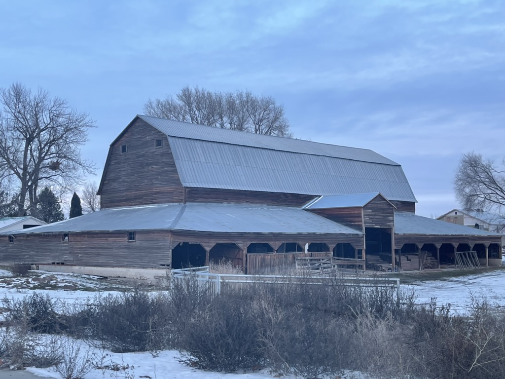 A weathered wooden barn with a metal roof and snow on the ground.